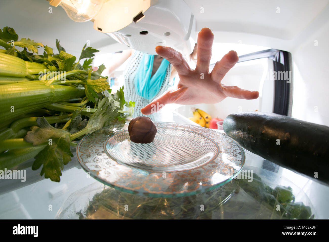 Lutte : régime alimentaire Une main attraper un petit bonbon dans le réfrigérateur ouvert plein de verts. Banque D'Images