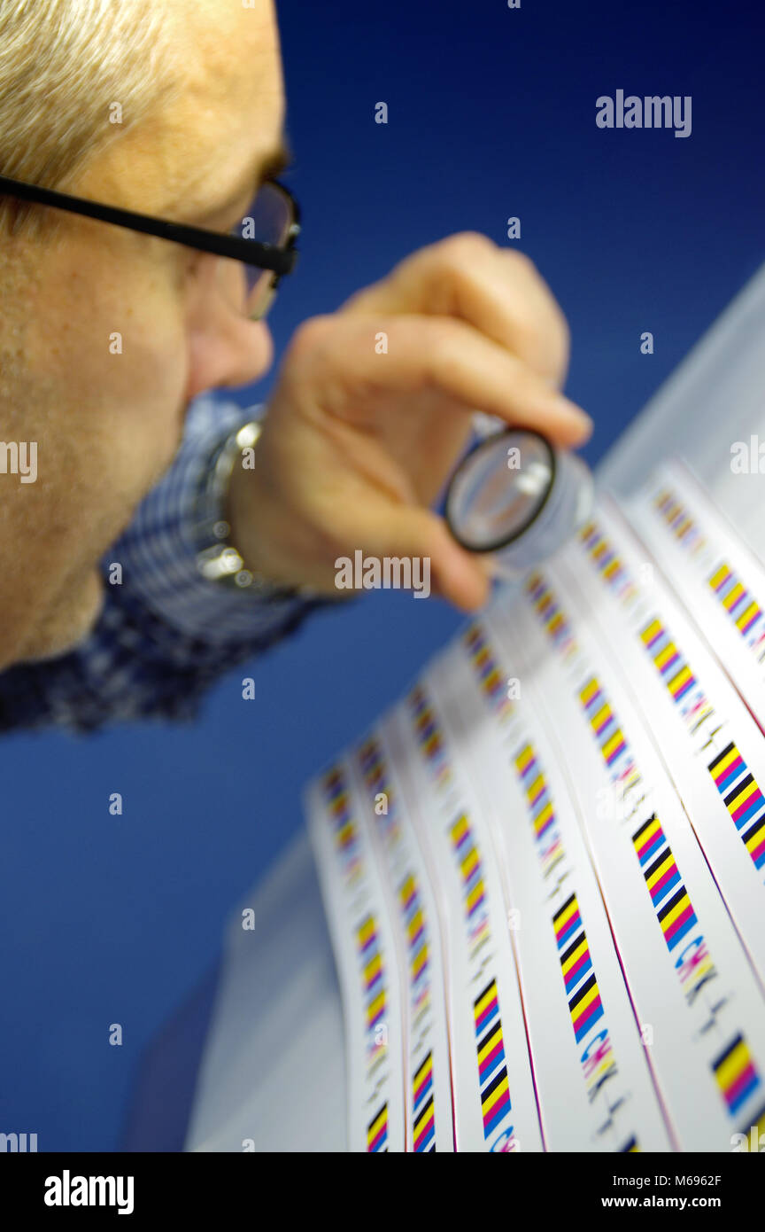 L'homme à l'aide de lentille loupe pour contrôler la qualité. Test d'impression CMJN le contrôle et l'immatriculation sur l'imprimé. Banque D'Images