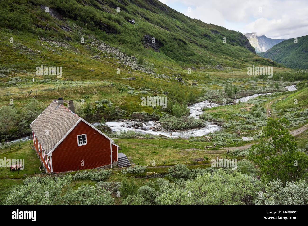 Chalet en bois rouge à côté d'un ruisseau de montagne dans une vallée au cours d'une journée nuageuse, près de la gare de Myrdal en Norvège Banque D'Images