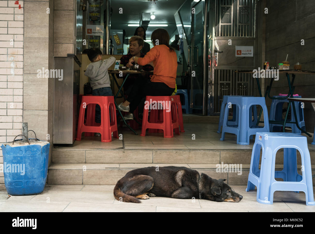 19 février 2018 - Tai O, Lantau Island, Hong Kong. La famille asiatique ayant un repas tandis que les chien allongé sur le rue. Banque D'Images