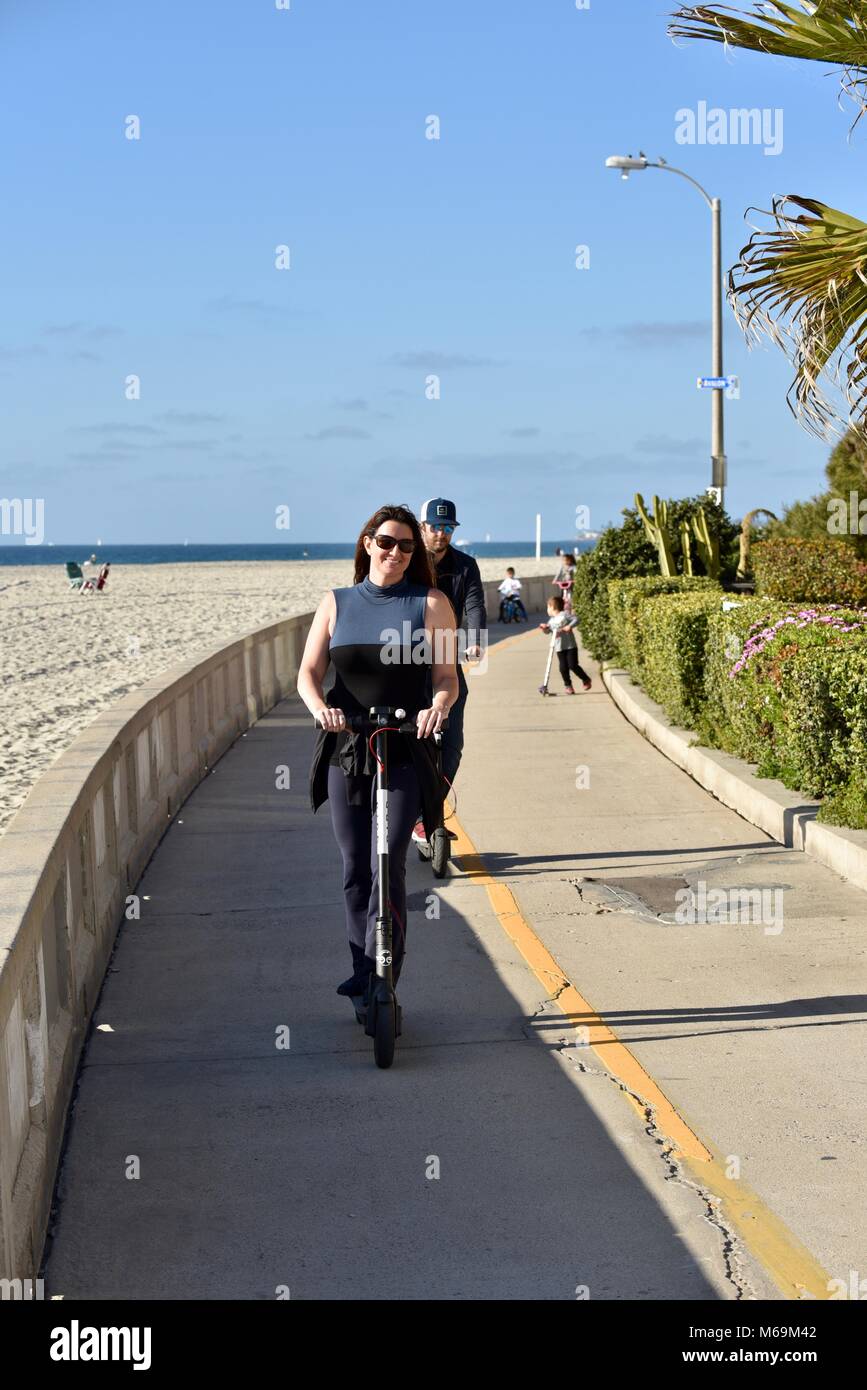 Woman riding sur tous les oiseaux-scooter électrique le long de la plage populaire promenade pavée de Mission Beach, San Diego, California, USA Banque D'Images