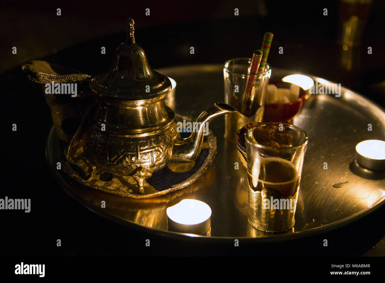 Pot de thé à la menthe marocain traditionnel et verres servis sur un plateau par la lumière de bougie, Marrakech, Maroc Banque D'Images