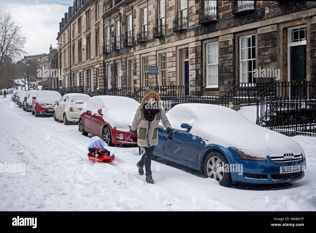 Une femme tirant un enfant sur une luge dans la neige à Stockbridge, Édimbourg. Banque D'Images