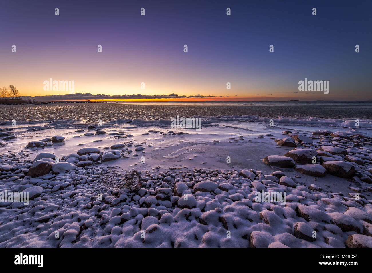 La neige a couvert des pierres sur un lac avec le coucher du soleil dans l'arrière-plan Banque D'Images