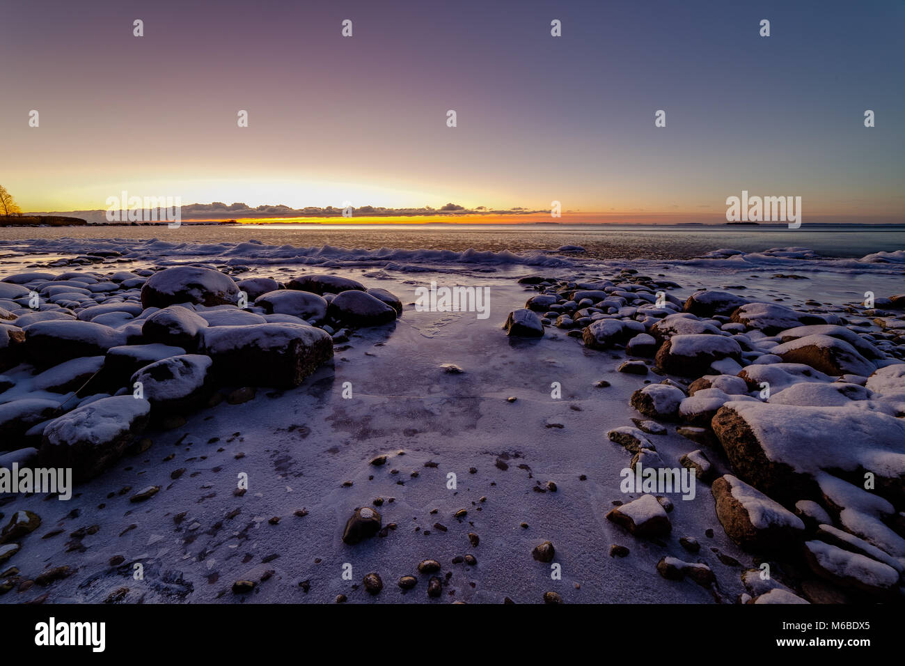 La neige a couvert des pierres sur un lac avec le coucher du soleil dans l'arrière-plan Banque D'Images