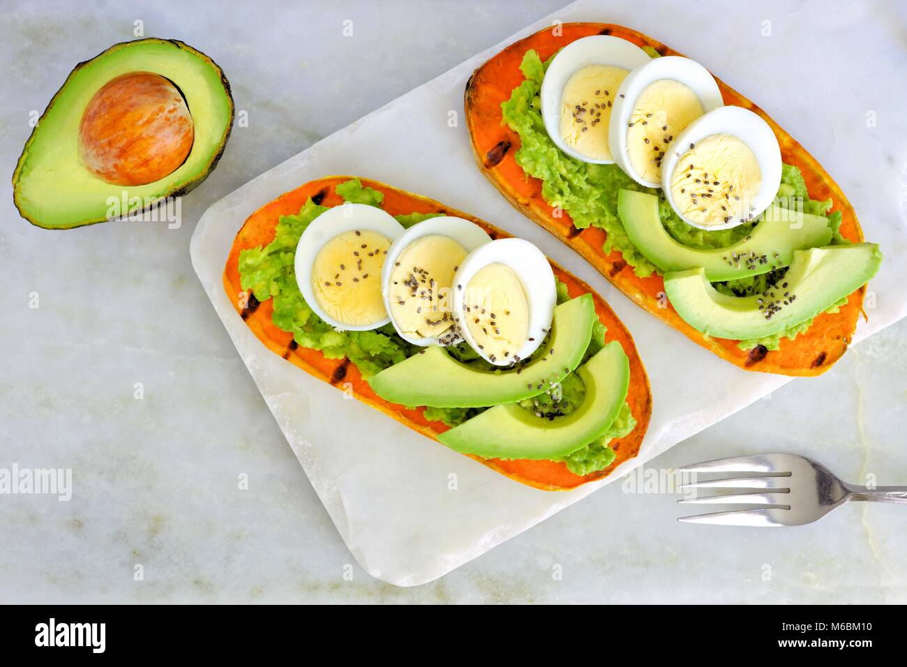 Toasts de pommes de terre avec de l'avocat, oeufs et chia graines sur un serveur en marbre. Vue de dessus sur un arrière-plan lumineux. Banque D'Images