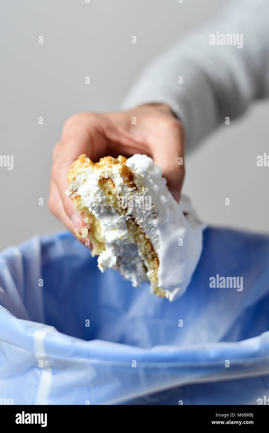 Libre d'un jeune homme de race blanche de jeter un morceau de gâteau garni de crème fouettée dans la corbeille Banque D'Images