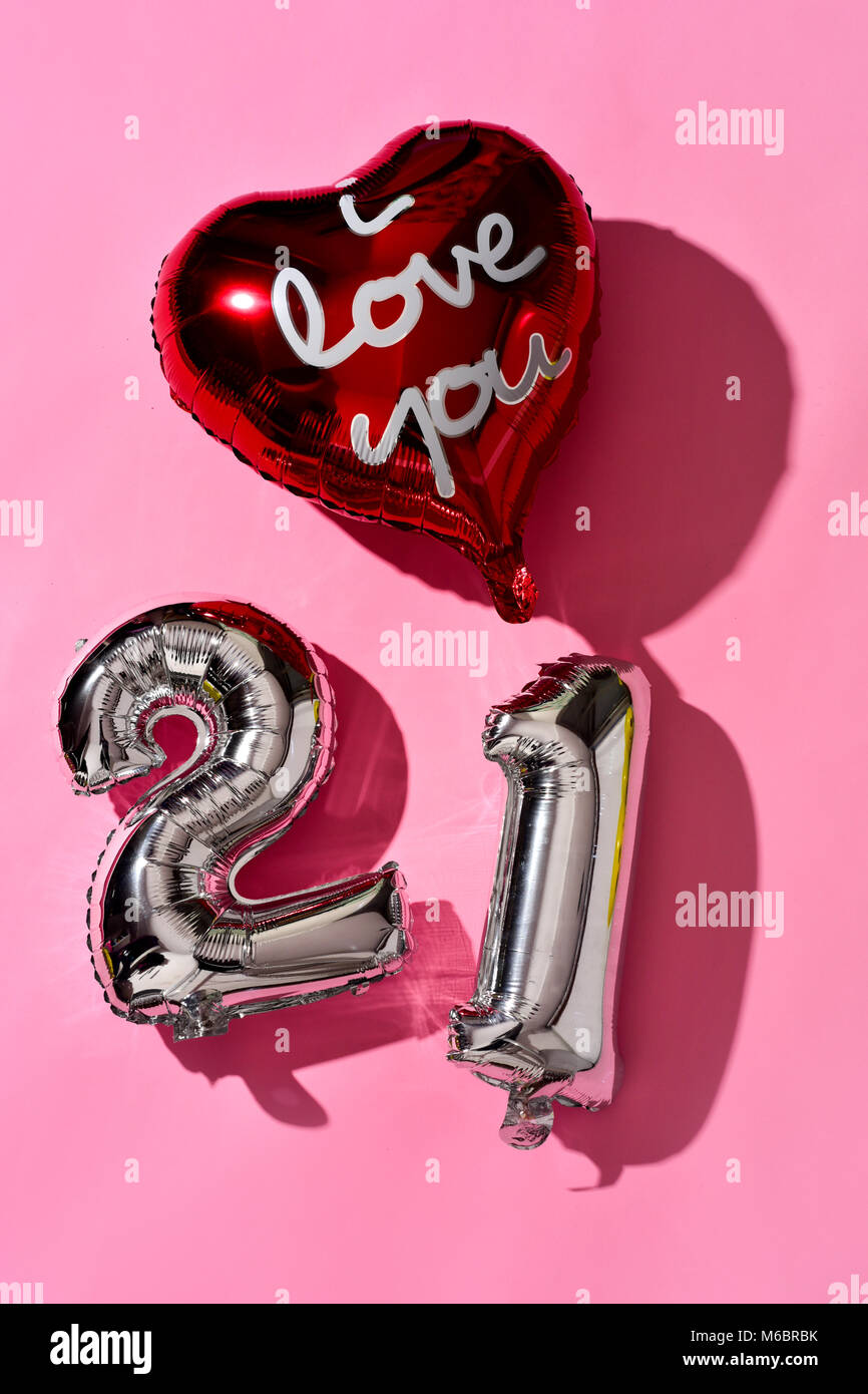 Un ballon en forme de coeur avec le texte je t'aime écrit en c et quelques ballons en forme de numéro argenté formant le numéro 21 contre un fond rose Banque D'Images