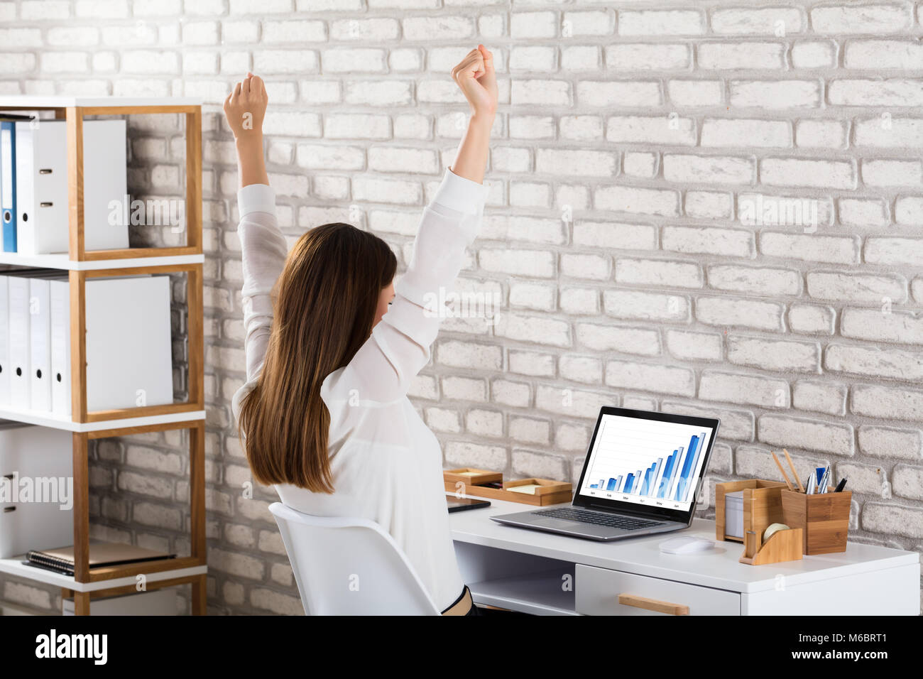 Succès Businesswoman Sitting on Chair élever ses mains avec le graphique sur un écran d'ordinateur portable Banque D'Images