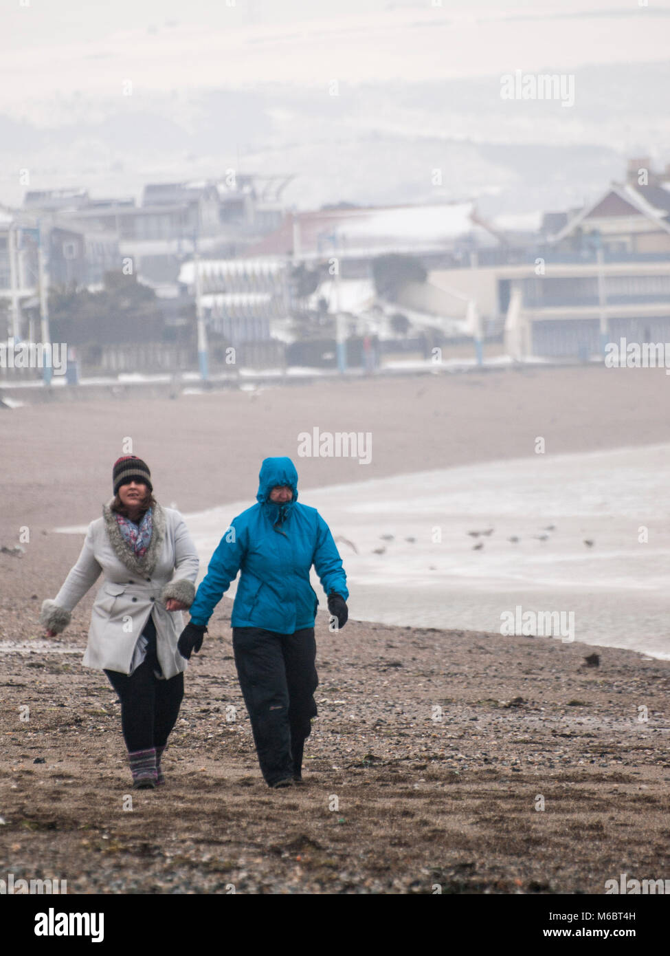 Un couple de personnes à pied sur la plage de Weymouth dans des vents violents et de la neige. Banque D'Images