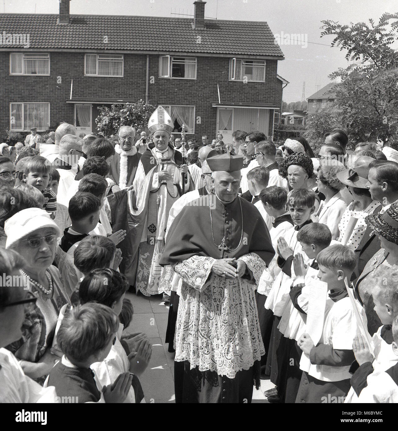 Années 1960, spectateurs adultes et enfants bienvenue la visite d'un évêque catholique romain de leur quartier, un nouveau domaine, de logement de style moderne années 60, Bucks, England, UK. Banque D'Images