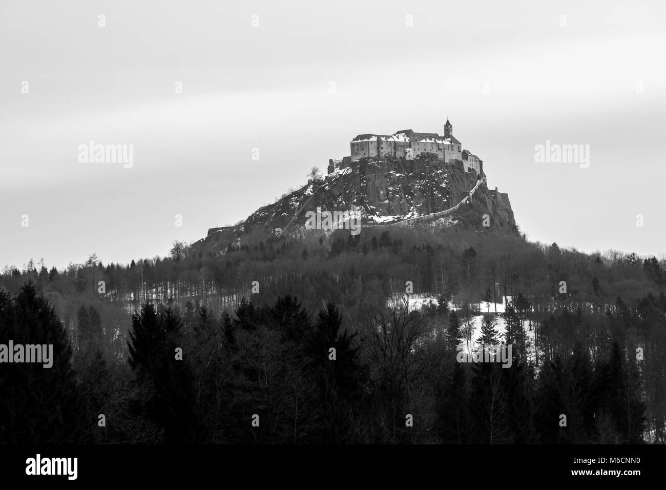 Décor noir et blanc avec la forêt en hiver et l'imposant château de Riegersburg vu dans la distance Banque D'Images