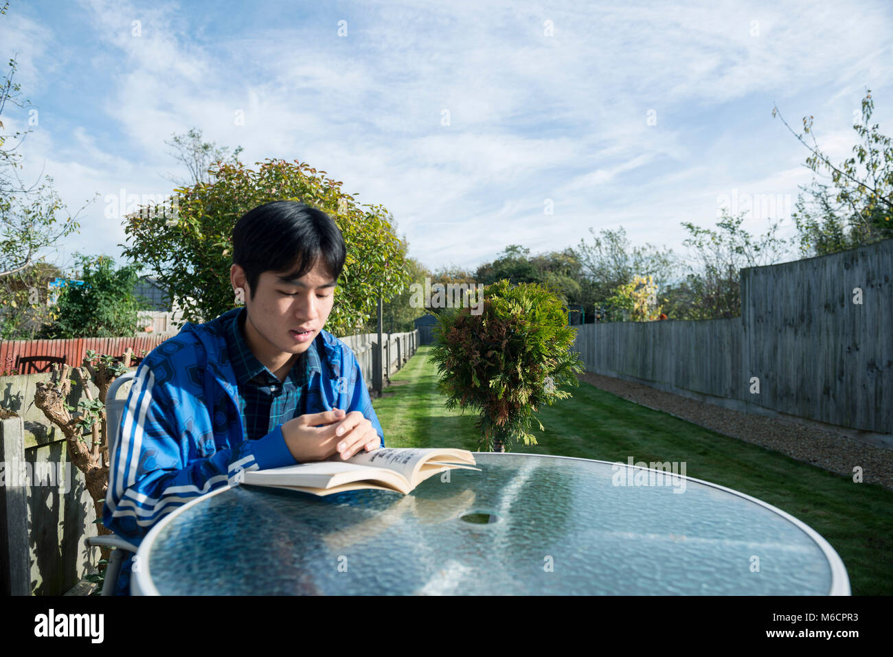 Un jeune étudiant asiatique se trouve à l'extérieur dans le jardin de la chambre d'étudiant la lecture d'un livre Banque D'Images