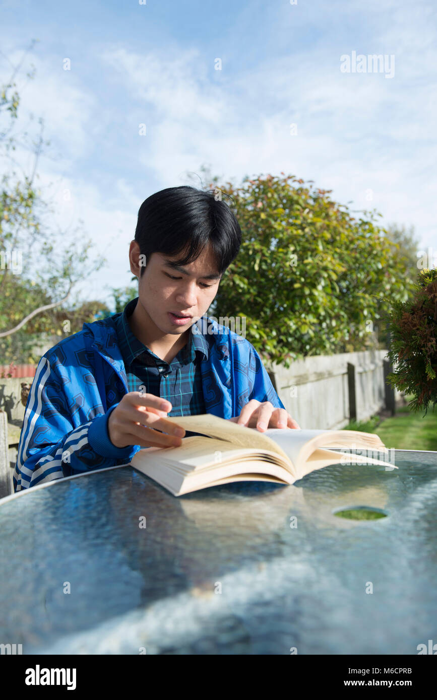 Un jeune étudiant asiatique se trouve à l'extérieur dans le jardin de la chambre d'étudiant la lecture d'un livre Banque D'Images