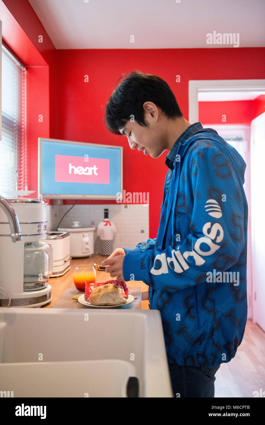 Un jeune étudiant international outre-mer asiatique obtient et prépare son déjeuner dans la cuisine de sa famille d'accueil home Banque D'Images