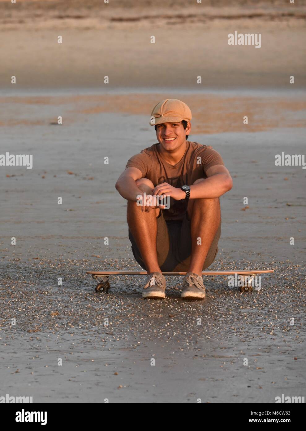 Hanche, jeune homme en faisant une pause, assis sur planche sur la plage pour regarder le coucher du soleil, faire de "haka" signe (chill out), à San Diego, Californie, USA Banque D'Images