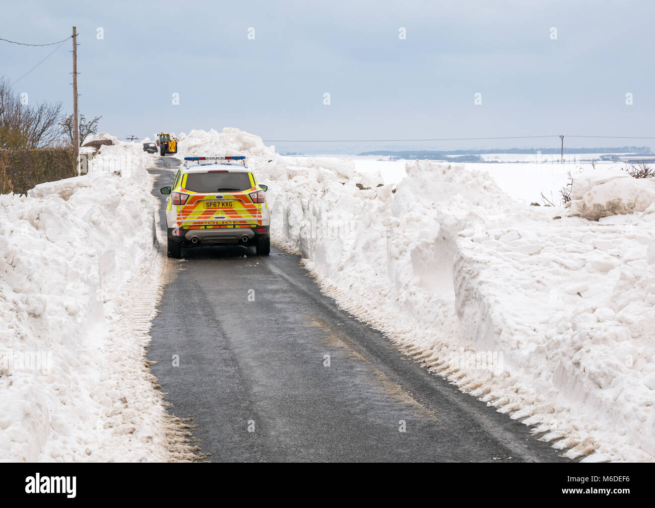 East Lothian, Ecosse, Royaume-Uni, le 3 mars 2018. Météo France : une route de campagne locale est fermé par un énorme banc de neige. Conseil d'un creuseur est l'élimination d'un grand banc de neige sur la route et une voiture de police est aussi présent. Banque D'Images