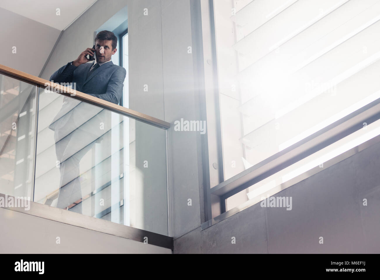 Businessman leaning on railing in office building et parler sur smartphone. Low angle shot personne d'affaires de passer un appel téléphonique. Banque D'Images