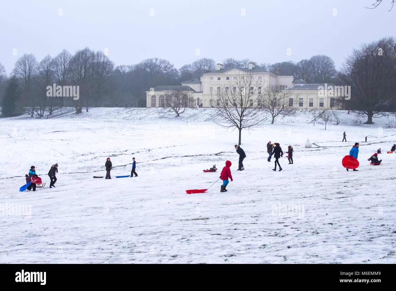 Les adultes et les enfants jouer dans la neige sur Hampstead Heath en face de Kenwood House à Londres après une chute de neige et de froid en hiver 2018. Banque D'Images