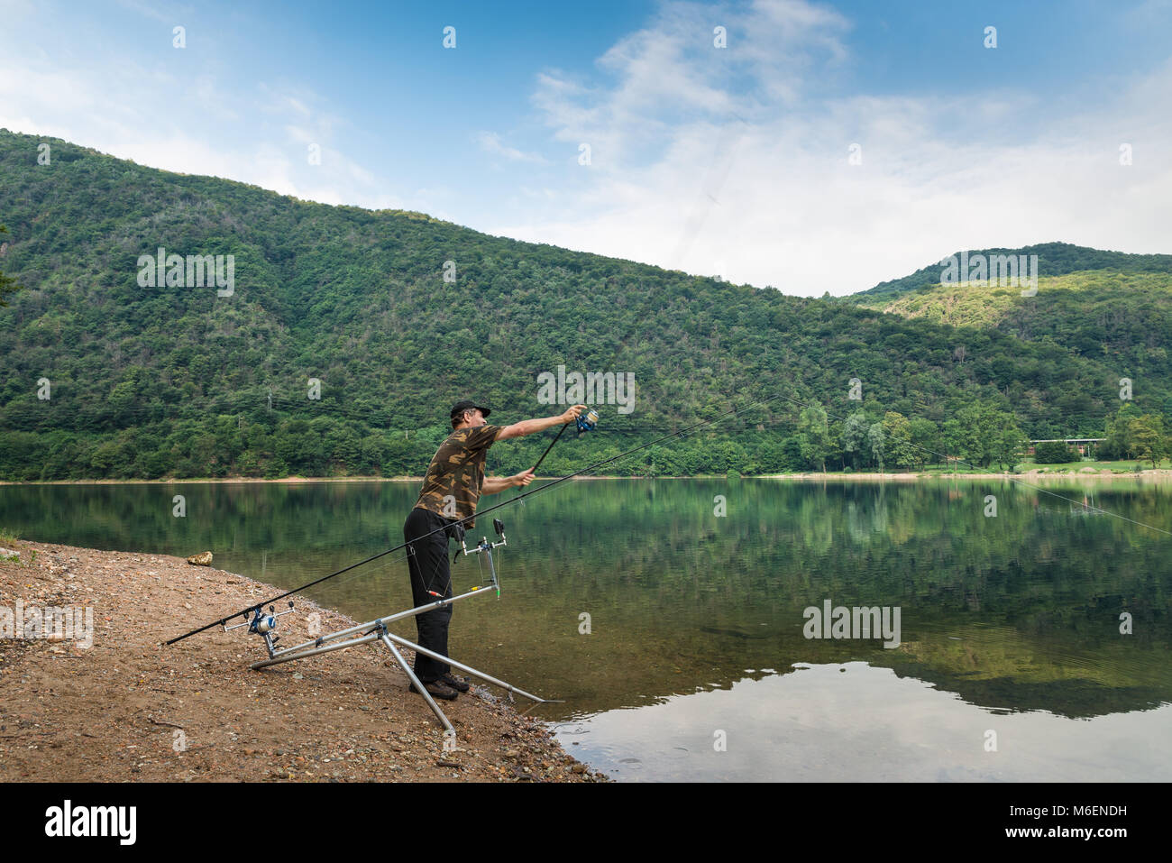 Aventures de pêche, pêche à la carpe. Angler avec t-shirt camouflage et une canne à pêche à la main, est l'appât casting Banque D'Images