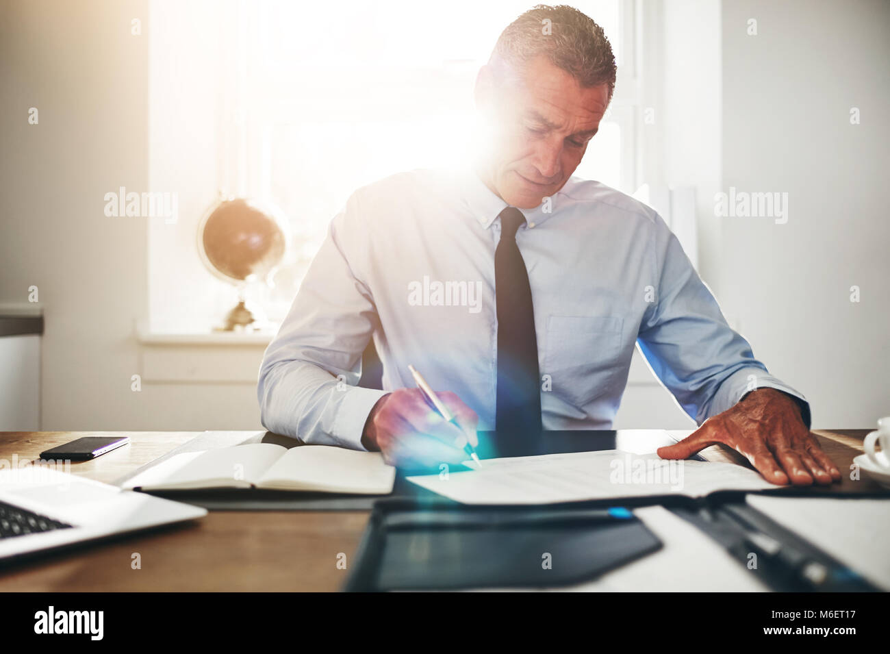 Mature businessman reading les formalités administratives et de l'aide d'un ordinateur portable tout en étant assis à son bureau dans un bureau Banque D'Images