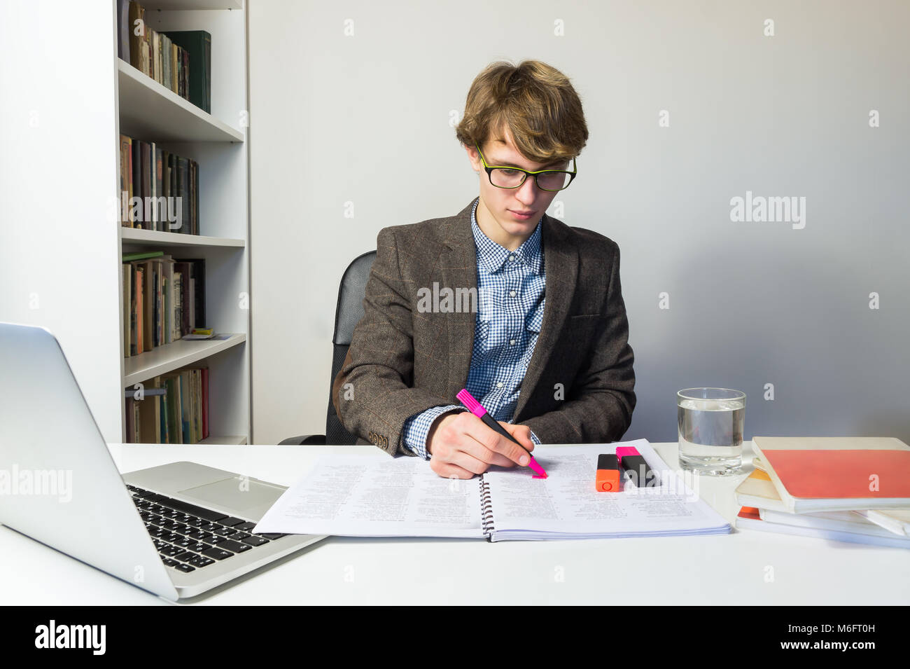 Jeune homme étudiant travaille avec des livres et un ordinateur portable sur accueil cession ou projet. Beau jeune personne dans la lecture lunettes à workp minimaliste moderne Banque D'Images