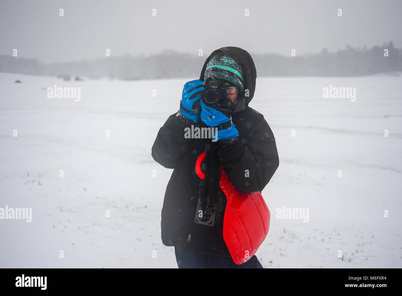 Un adolescent prend des photos avec un Fuji XT1 une tempête de neige dans le New Forest Hampshire Angleterre vêtus de vêtements chauds pour l'hiver et des gants. Banque D'Images