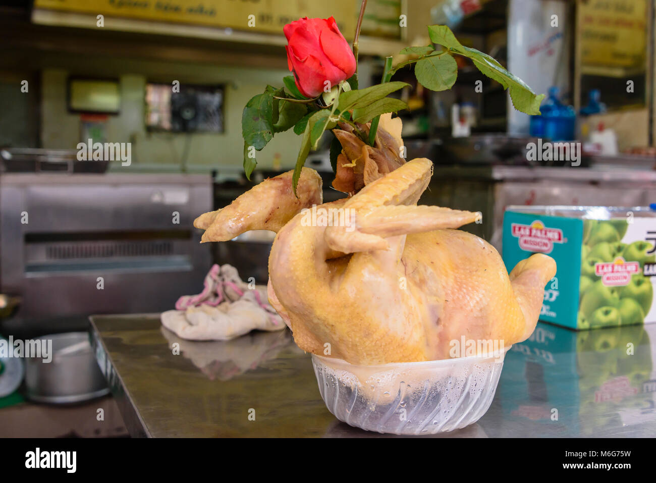 Une carcasse de poulet avec une rose rouge coincé sa gorge sur une table à l'extérieur d'un restaurant à Hanoi, Vietnam Banque D'Images