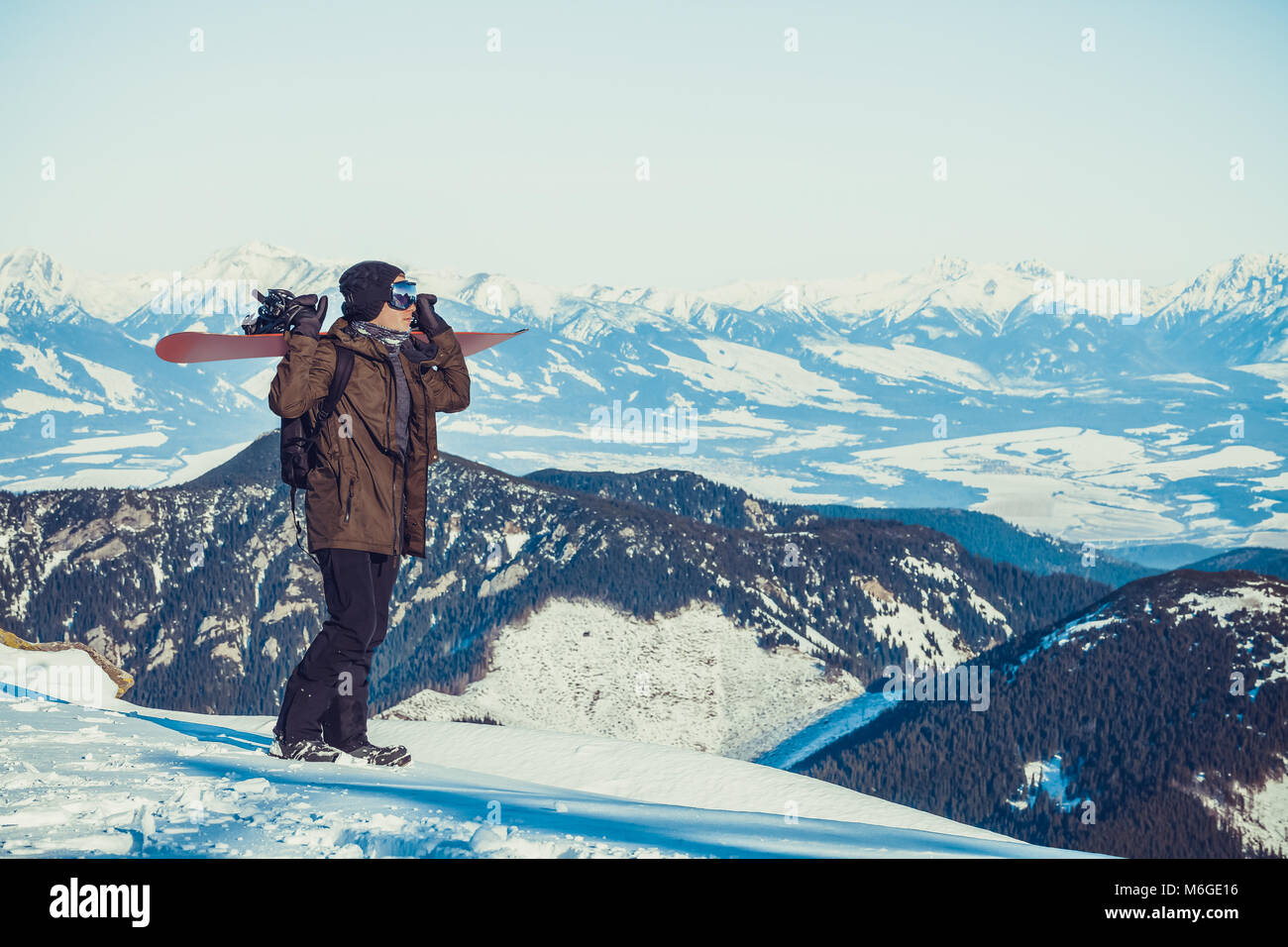 Snowboarder debout au sommet d'une montagne, le holding snowboard sur son épaule et profiter de beaux paysages devant lui Banque D'Images