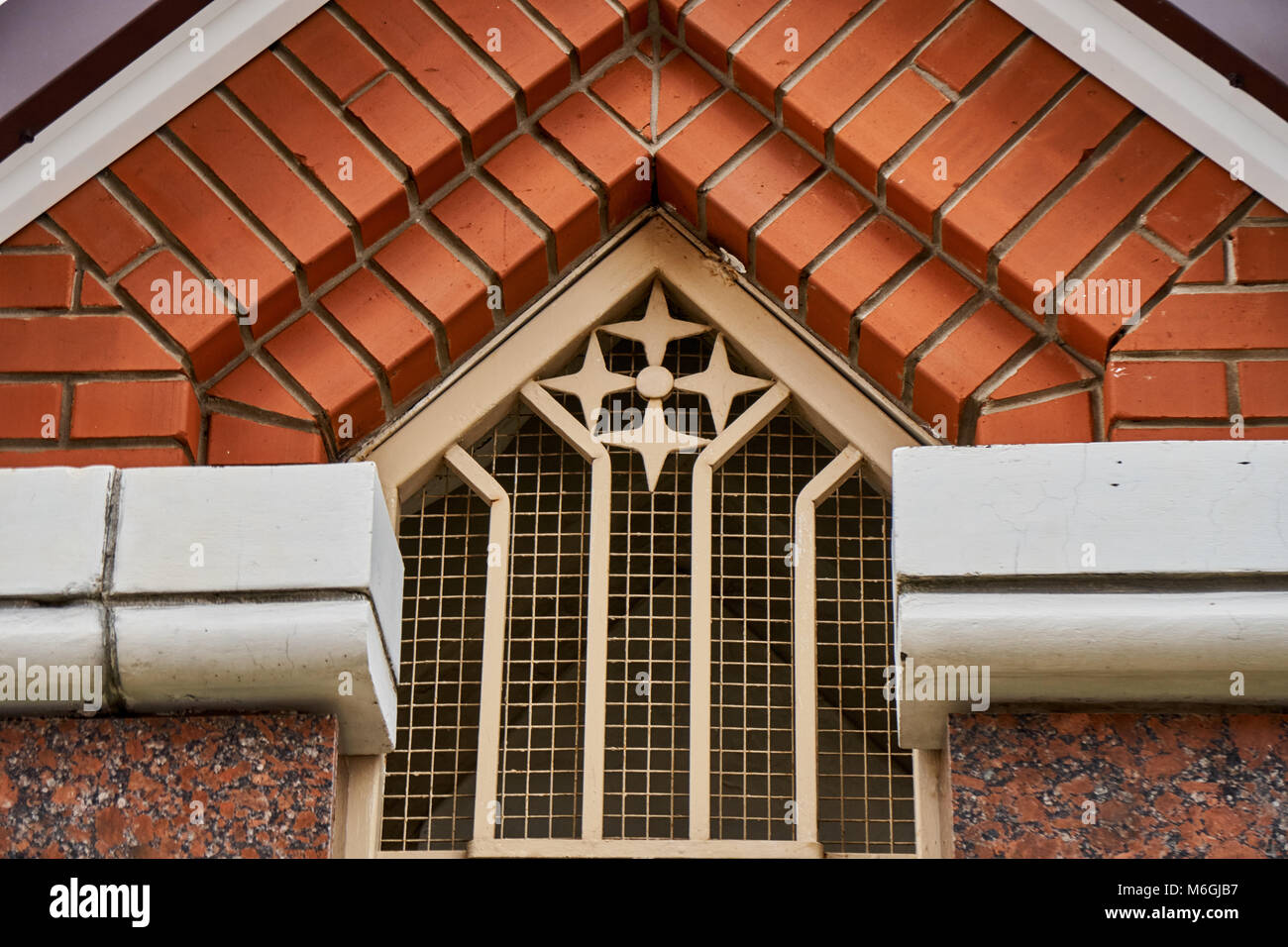 Treillis figuré élégant avec décorations sur la fenêtre située sous la mezzanine de toit en brique partie de la façade du bâtiment de cottage Banque D'Images