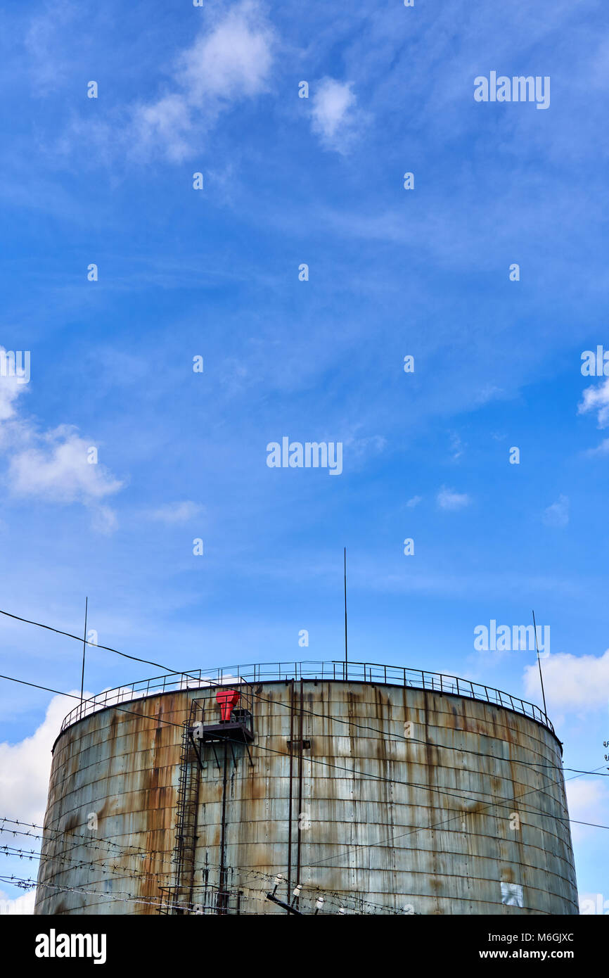 Vieux réservoir de stockage de carburant industriel rouillé contre ciel bleu nuageux Banque D'Images