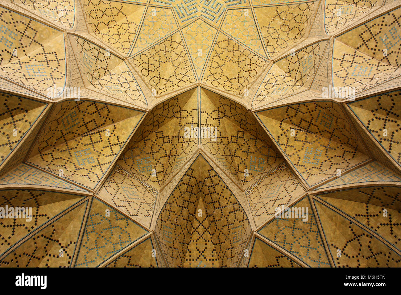 De façon complexe et magnifiquement décorée dans des tons chauds de jaune au plafond avec des tons de bleu dans une mosquée musulmane à Esfahan / Isfahan, Iran. Banque D'Images