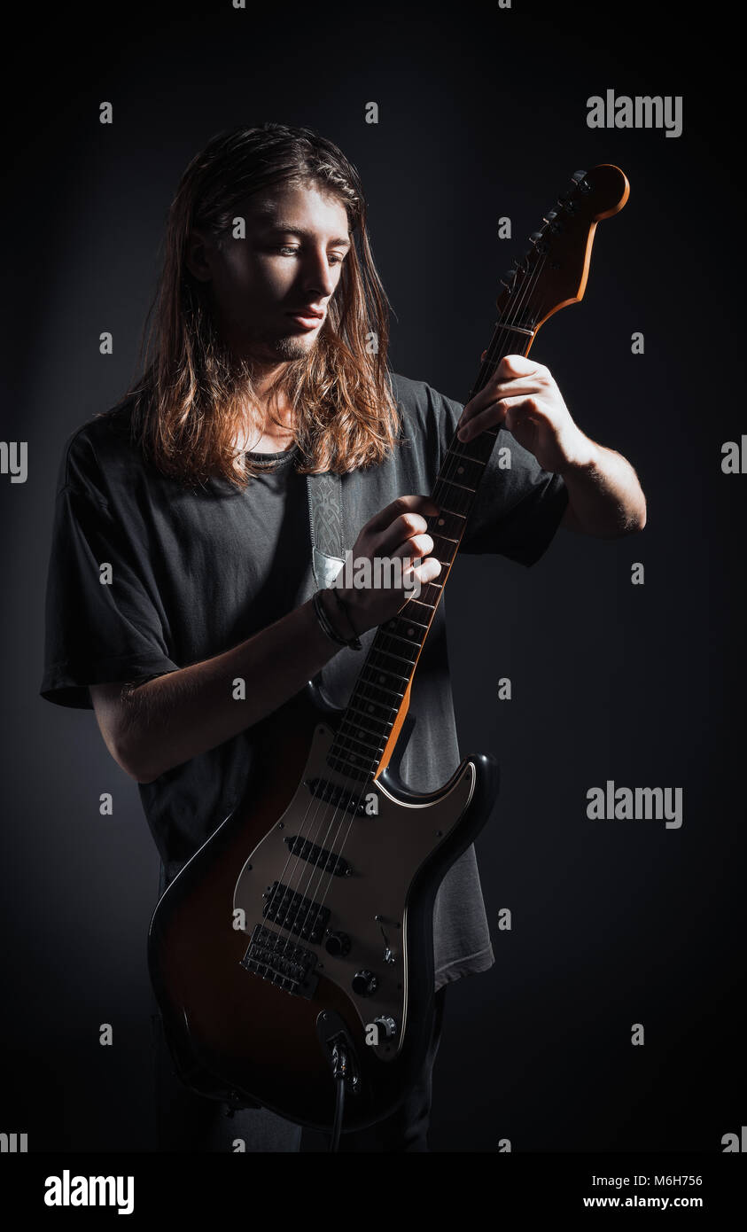 Portrait studio dramatique : un beau jeune homme musicien (rock) avec des cheveux longs à jouer de la guitare électrique Banque D'Images