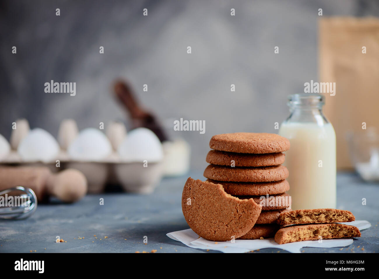 Oatmeal Cookies dans une pile avec une bouteille de lait et des ingrédients hors focus. Concept de cuisson en high key avec copie espace. Banque D'Images