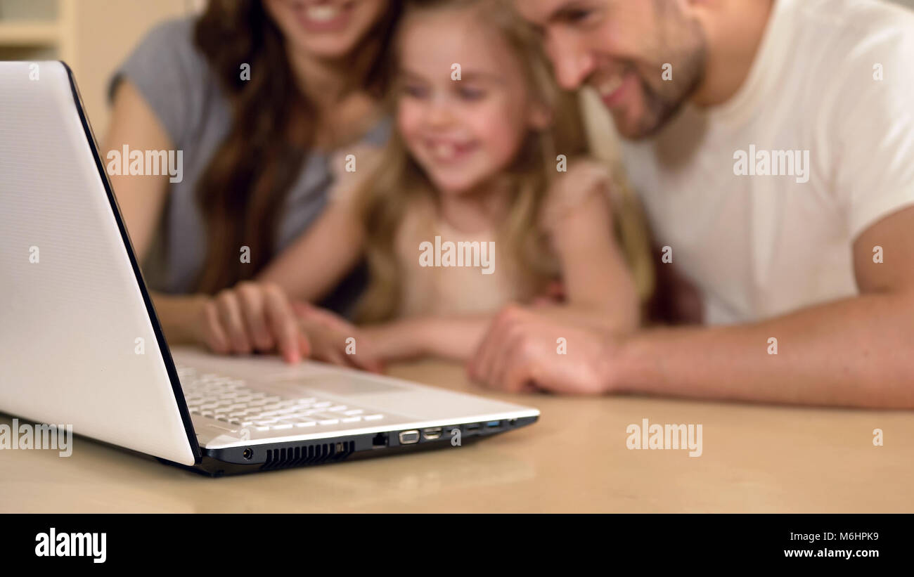 Heureux parents et fille looking at laptop, girl enjoying l'enseignement à distance Banque D'Images