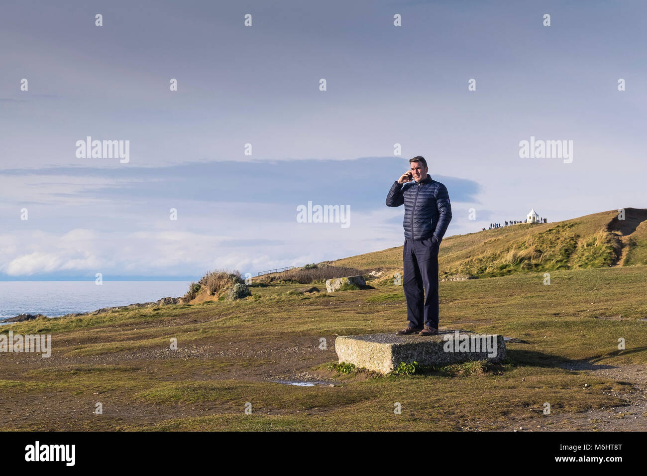 Un homme debout sur un bloc de pierre en utilisant son téléphone mobile à dans Fistral Newquay Cornwall. Banque D'Images