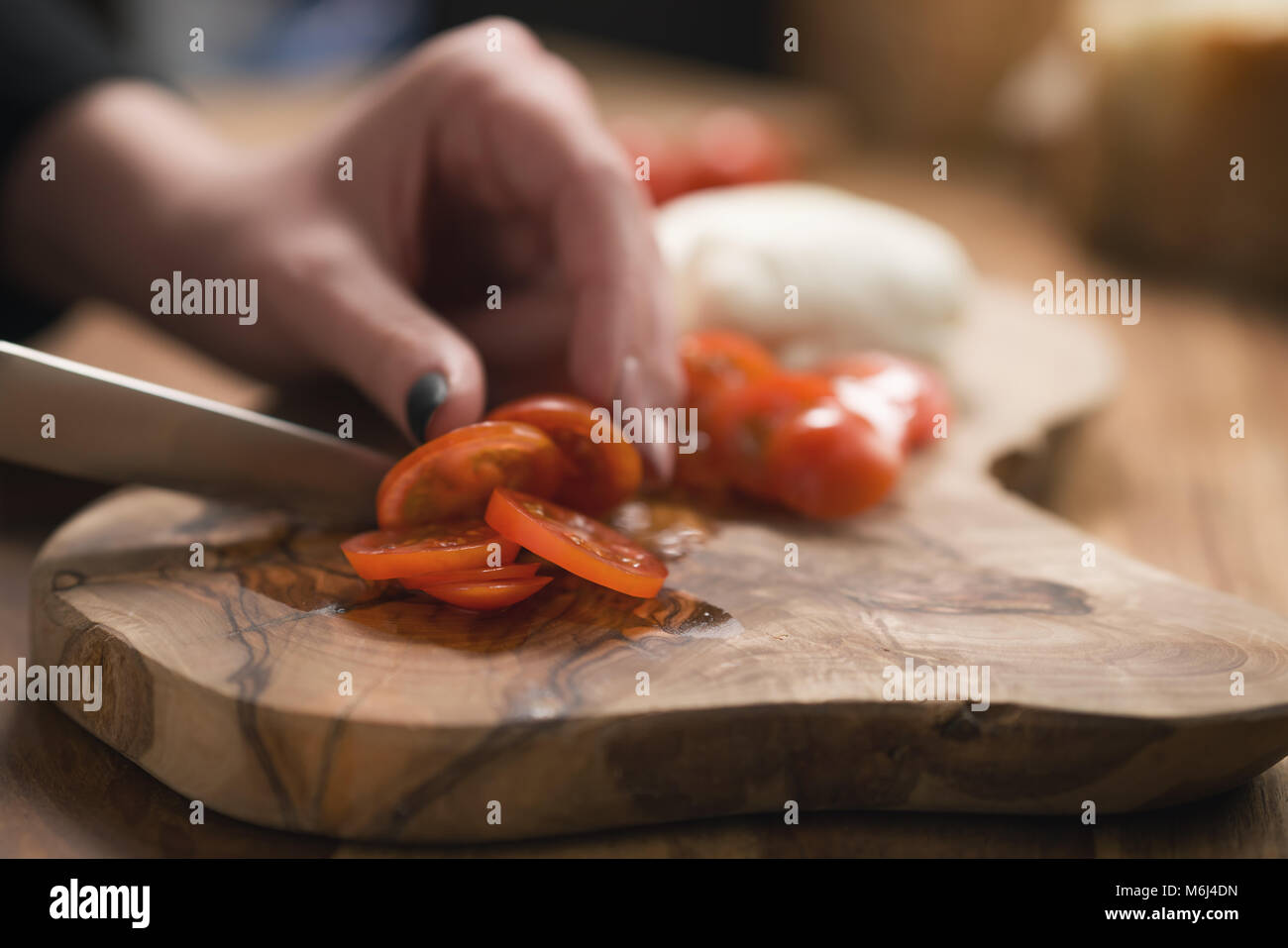 La main de l'adolescence féminine de trancher les tomates cerise avec un couteau sur planche de bois Banque D'Images