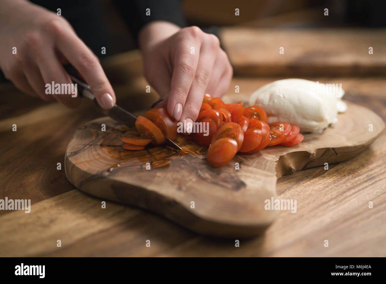 La main de l'adolescence féminine de trancher les tomates cerise avec un couteau sur planche de bois Banque D'Images