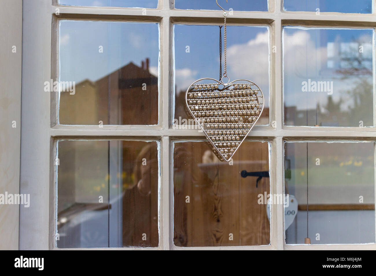 Un joli coeur couleur argent est suspendu à l'extérieur d'une fenêtre à guillotine sur une maison de Saffron Walden, Essex, UK Banque D'Images