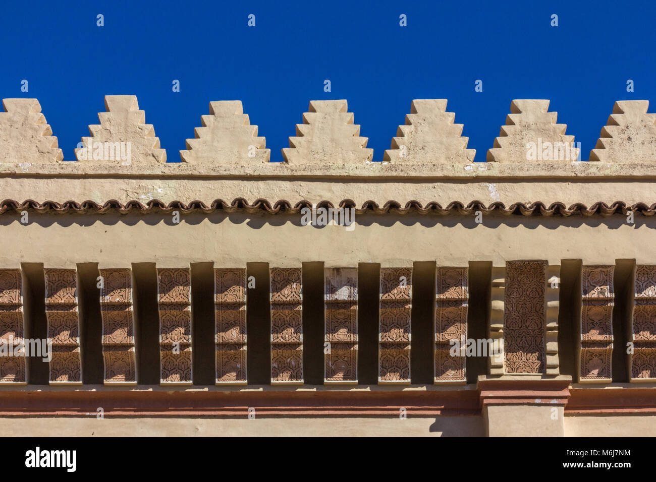 Détail architectural de merlons au-dessus des rangées de corbeaux sur la Mosquée de la Kasbah, contre un ciel bleu foncé. Banque D'Images