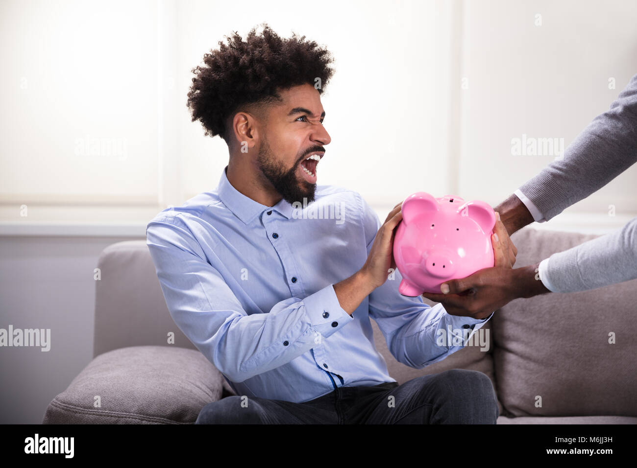 Jeune homme dynamique assis sur le canapé se battre pour la Pink Piggybank Banque D'Images