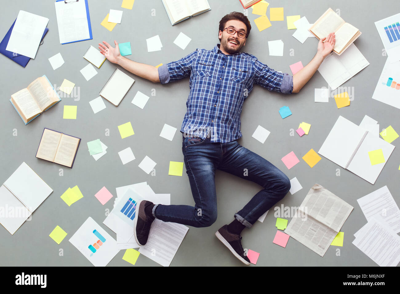 Jeune homme isolé sur fond gris avec des papiers et notes joyeux sourire Banque D'Images