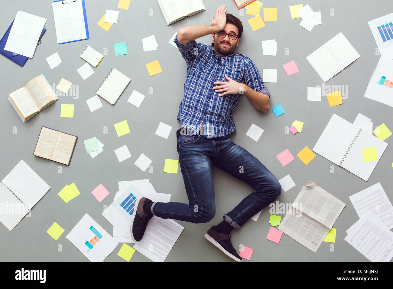 Jeune homme isolé sur fond gris avec des papiers et notes sleepy Banque D'Images