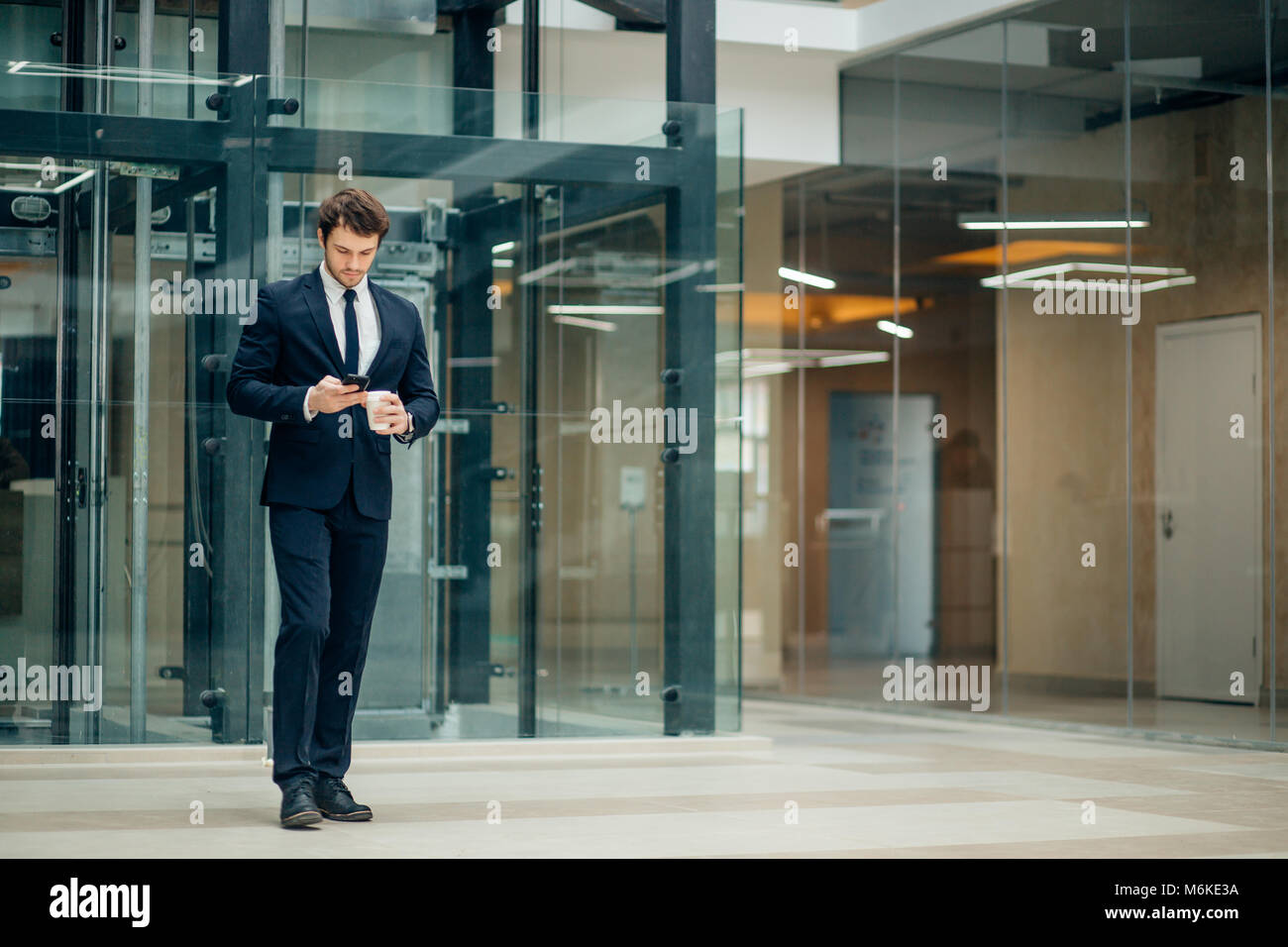 Homme d'affaires en costume noir de boire du café à emporter et utiliser phone Banque D'Images