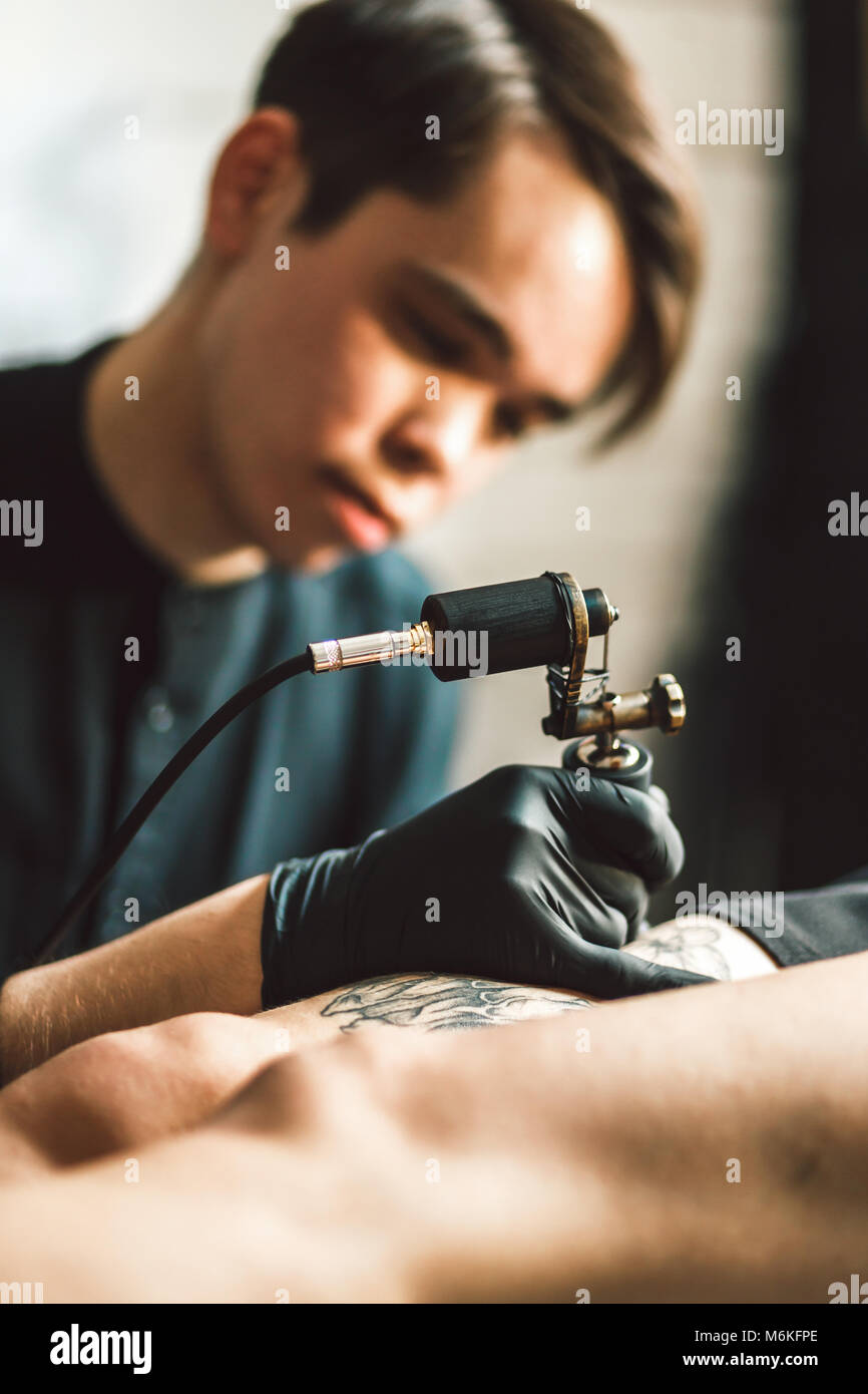 Artiste masculin de tatouage fait un tatouage sur la jambe d'une femme. Banque D'Images