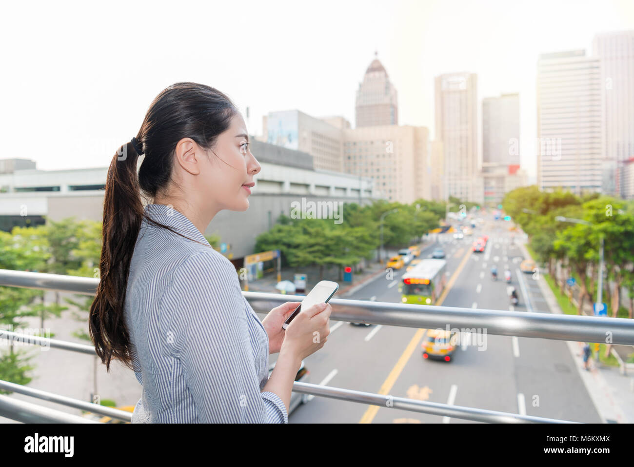 Beau bureau dame debout à l'extérieur de l'office avec la pollution de l'air mauvais et la tenue d'une application pour smartphone pour tester l'AQI. Banque D'Images