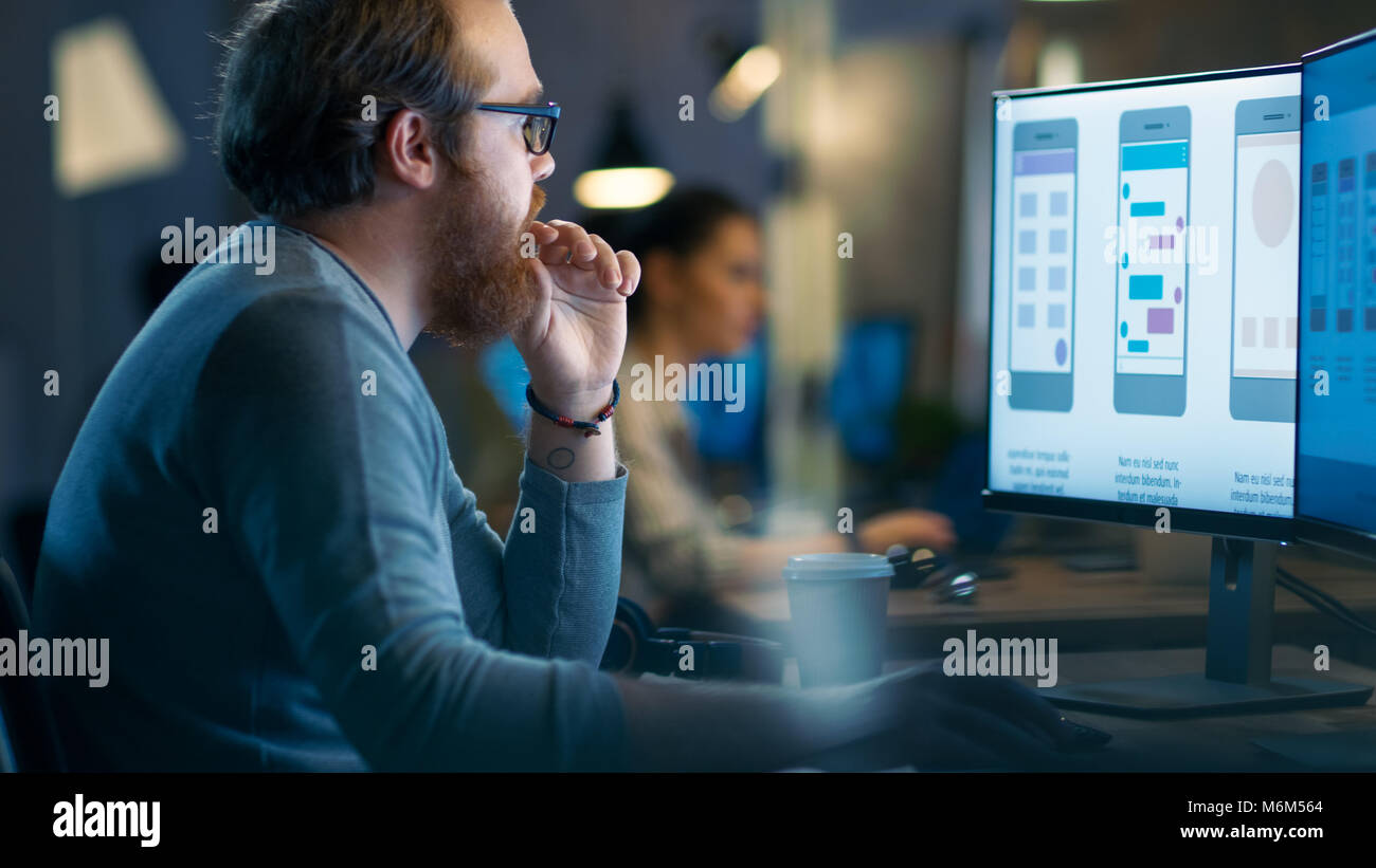 Développeur d'applications mobiles mâle travaille avec des graphiques sur son ordinateur personnel avec deux moniteurs. Il partage Loft Bureau avec d'autres personnes créatives. Banque D'Images