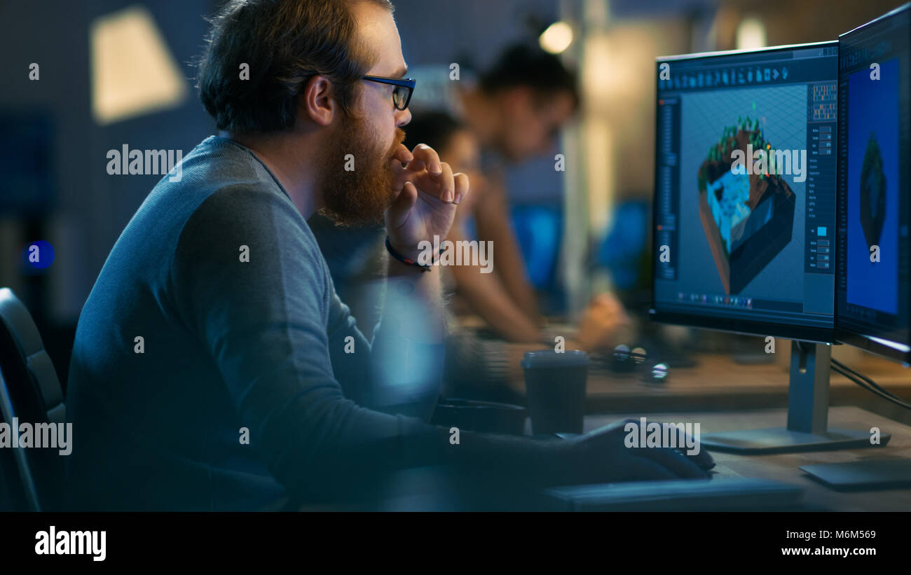 Développeur de jeux de sexe masculin travaille sur un niveau Design de son ordinateur personnel avec deux écrans. Il travaille dans un environnement de bureau avec des créateurs de talent très Banque D'Images