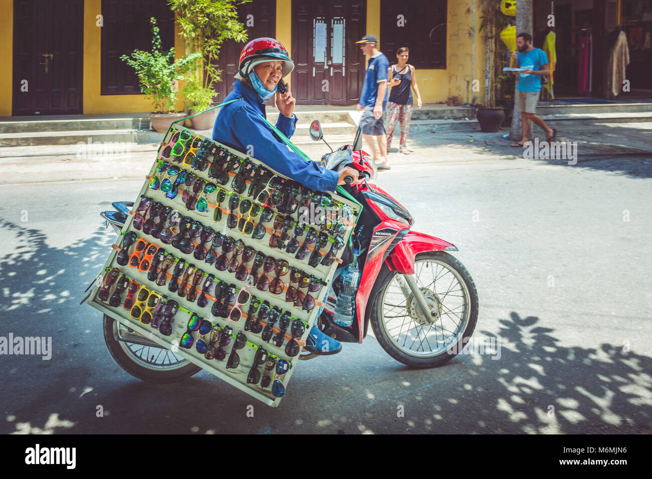 Un commerçant d'une grande sélection de lunettes de soleil sur une mobylette  dans les rues de Hoi An, Vietnam Photo Stock - Alamy