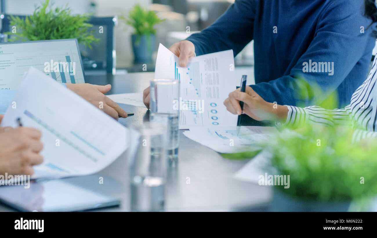 Tiré de l'entreprise Salle de réunion Table avec les gens pour le partage de documents avec les graphiques en secteurs et les statistiques, tablettes et écrans portables. Banque D'Images